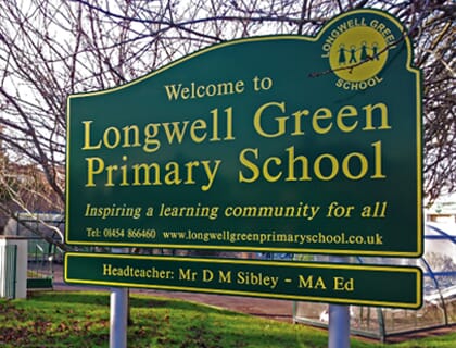 A green school sign with a separate headteacher sign